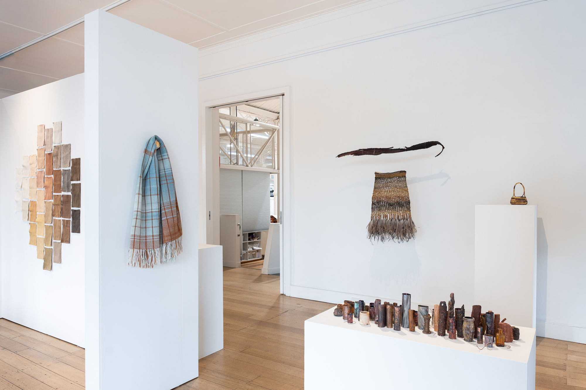 An exhibition space filled with earth-toned artworks, textiles, ceramics, and woven forms.