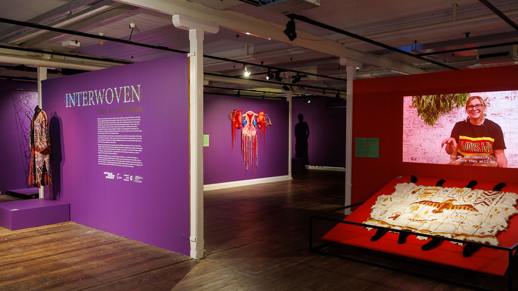 A gallery with dark purple walls and textile artworks